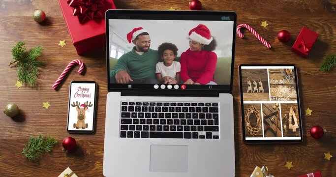 Family wearing snatas hats on video call on laptop, with smartphone, tablet and decorations