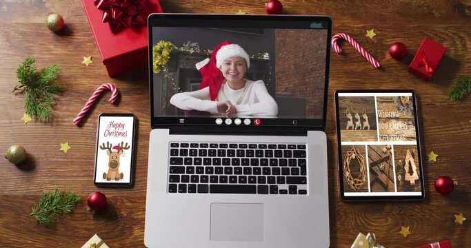 Caucasian woman in santa hat on video call on laptop, with smartphone, tablet and decorations