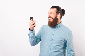 Happy beard man is using his phone and ear pods over white background.