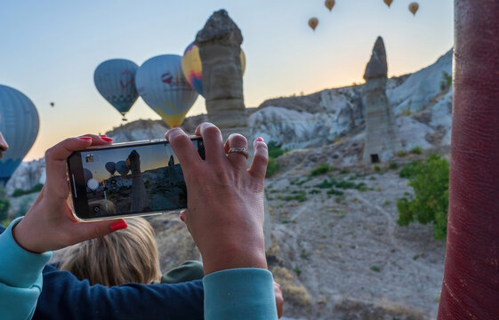 Young female taking pictures of air balloons by cell phone or mobile in Cappadocia, Turkey of Hot air balloon during flight or flying