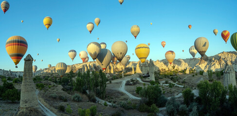 Panorama of bunch of colorful hot air balloon flying early morning in Cappadocia, Turkey against typical rock formation due to volcanic activity in love valley located in Goreme national park - Powered by Adobe