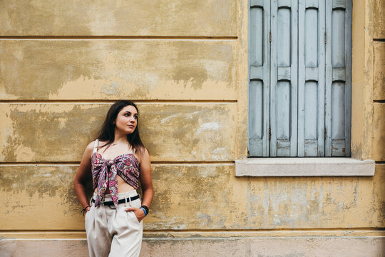 Girl perched on a yellow wall. Relaxing tourist near an Italian-style building