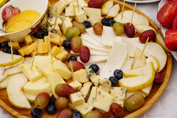 cheeses with grapes, dried fruits, nuts, honey and jam on a round wooden plate.