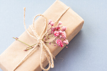 Gift box in kraft paper with pink flowers on blue background. Space for text. Handmade gift for woman. Closeup