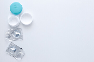 A container for lenses and two sealed lenses lie on the side on a white background with space for text. top view, flat lay, copy space, isolate