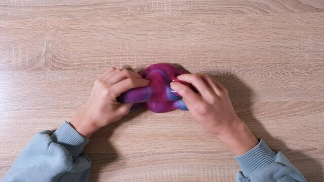 Playing with slime, stretching the gooey substance for fun and stress relief. Close up and top view of female hand holding blue, pink and purple shining slime and squeezing it. 4K video.