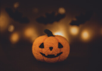 Woolen felted halloween pumpkin on a dark background. Jack o Lantern head with bokeh lights.