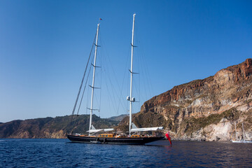 Lipari island (Aeolian archipelago), Messina, Sicily, Italy, 08.12.2021: view of the rocky seacoast with a big sailing ship in the foreground.