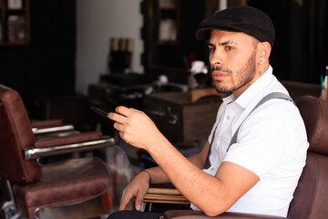 Barber playing with the scissors in his hands sitting in his barbershop chair. Man with cap.