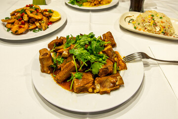 Delicious plate of Chinese style edo pork ribs with sauce and lots of coriander served in a restaurant with white tablecloths