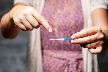 girl holding a positive pregnancy test in her hands on a gray background