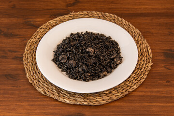 Portion of black rice paella with prawns and squid on a white plate and esparto placemat