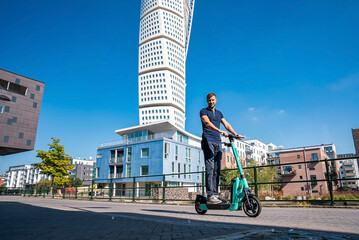 Young man riding an electric scooter down the streets in Malmo. Ecological transportation concept. Sideways man riding an e-scooter © Aerial Film Studio