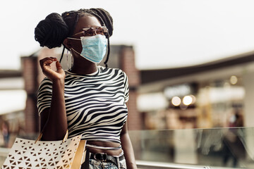 Young african american woman, wearing protective mask at mall, woman with shopping bags shopping