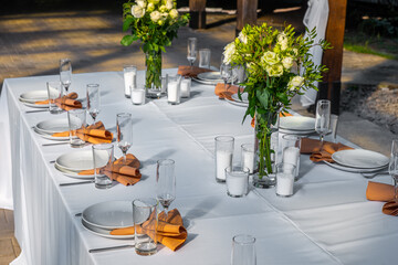 Wedding table setting decorated with fresh flowers in a brass vase. Wedding floristry. Banquet table for guests outdoors with a view of green nature. Bouquet with roses