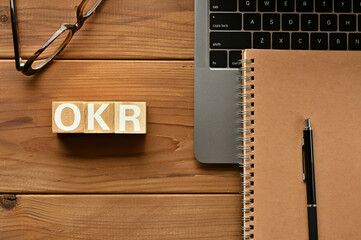On the table there is a word cube lined OKR with laptop computers and glasses. It is an...