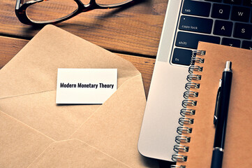 On the table, there is a card with the word of Modern Monetary Theory along with a laptop computer...