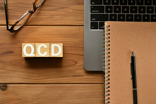 On the table there is a word cube lined QCD with laptop computers and glasses. It is an abbreviation for the word Quality, Cost, Delivery.