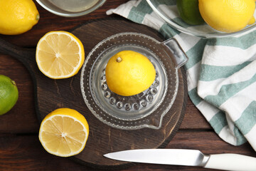 Glass squeezer and fresh lemons on wooden table, flat lay