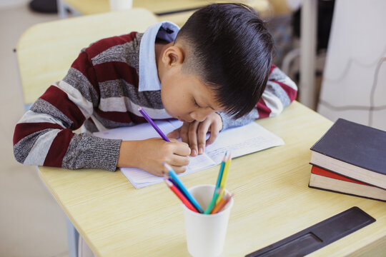 Serious Asian elementary shool boy studying in the shcool desk
