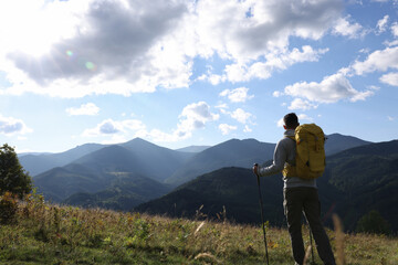 Obraz premium Tourist with backpack and trekking poles enjoying mountain landscape, back view. Space for text