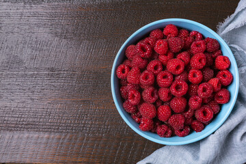 Red raspberry berry in plate on wooden table.