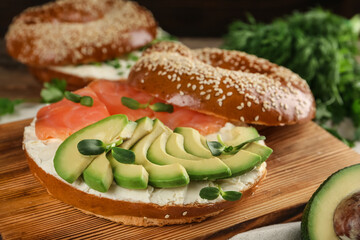 Delicious bagel with cream cheese, salmon, avocado and microgreens on wooden board, closeup