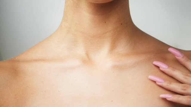 Young woman touching clavicles close-up, model with smooth healthy skin. Female shoulders, naked body. Beauty and body care concept. Unrecognizable person with bare neck and chest on white background.