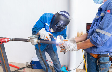 The welder in a welding mask welding steel pipe in liquid line.