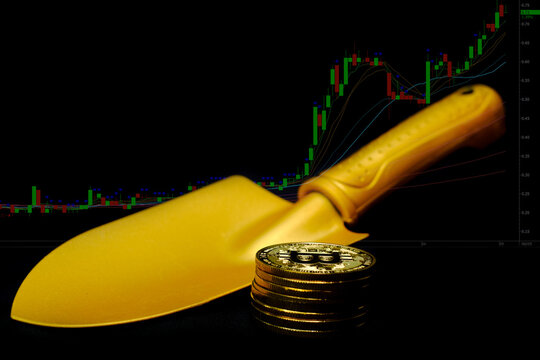 Gold bitcoin coins with a golden shovel at computer trading chart background