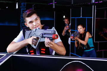 Fototapeta na wymiar Portrait of excited happy cheerful smiling guy with laser pistol playing laser tag in arena