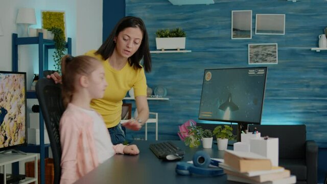 Child playing video games while mother interrupting play for homework and school tasks. Parent stopping action game on computer for little girl to learn for online courses and lessons