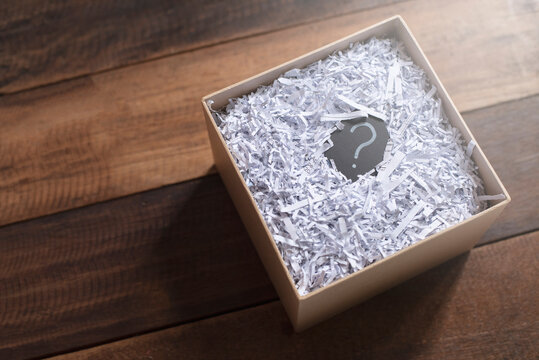 Question mark in a box with shredded paper on wooden table. Concept of suprise, delivery, shipment and questions