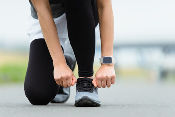 靴紐を結ぶびトレーニングの準備（スマートウォッチをつけた手元・女性）