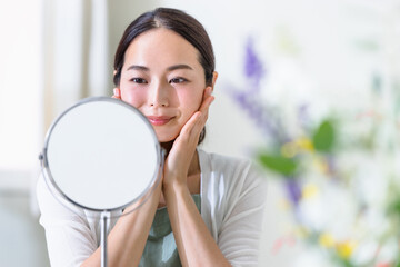 鏡を見てスキンケアをする女性（ビューティーイメージ）