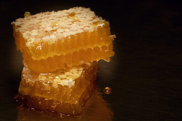 Honey in combs. On black background it is flowing on table. Excellent treat and original present.
