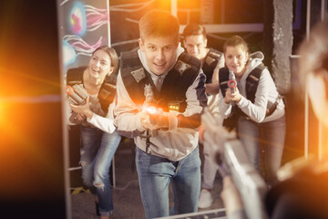 Obraz premium Portrait of happy young man with laser pistol and playing laser tag with his friends in dark room. High quality photo
