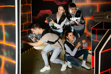 Fototapeta na wymiar Positive young people posing with laser guns having fun on dark lasertag arena