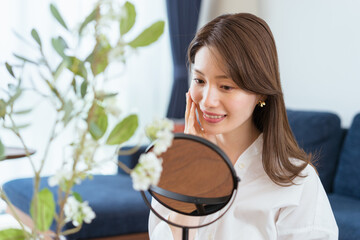 鏡を見てスキンケアをする女性（ビューティーイメージ）