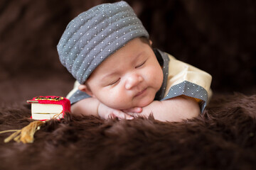 A cute Asian infant Muslim in thobe with prayer cap on bed in home, translation is noble quran