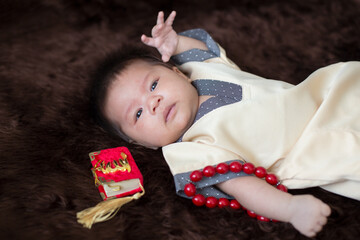 A cute Asian infant Muslim in thobe and rosary beads on red, muslim bead on bed in the home, translation is the name of muslim God "Allah" in arabic text