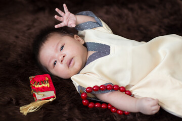 A cute Asian infant Muslim in thobe and rosary beads on red, muslim bead on bed in the home, translation is the name of muslim God "Allah" in arabic text