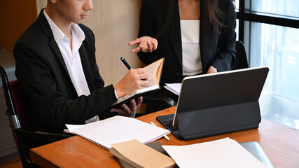 Cropped shot disabled businessman in wheelchair discussing business data with colleague in office.