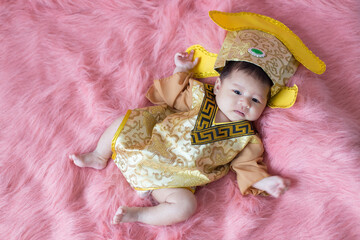 A newborn baby wearing a Chinese emperor's costume gold colour lying on a pink blanket.