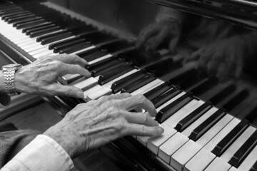 Hands of an old musician playing music on the keyboard of a grand piano, black and white image,...