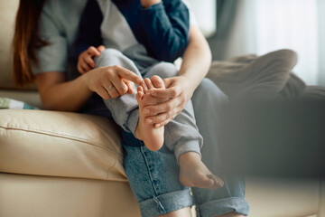 Close-up of mother touches toes of her barefoot child at home.