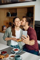 Happy couple in love takes selfie while having breakfast together at home.