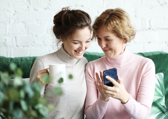Family, people and technology. Aged woman and her adult daughter using smartphone at home.