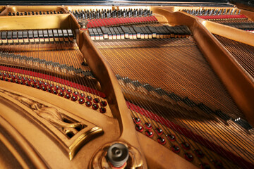 Inside an older grand piano with golden painted metal frame, strings, hammer, damper and red felt,...