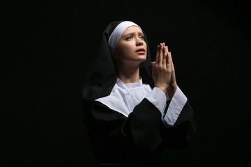 Young praying nun on dark background